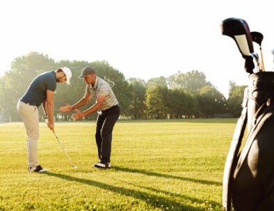 Young sportsman practicing golf with his teacher while standing on a green course
