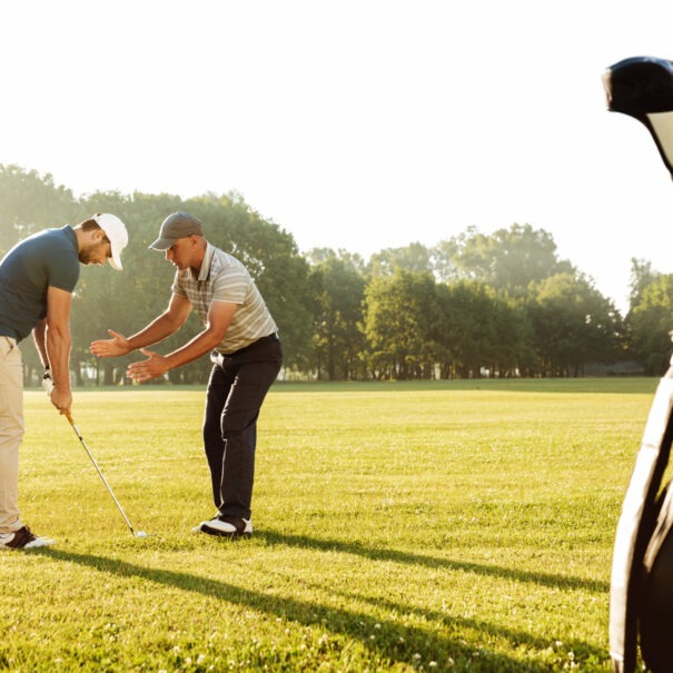 Young sportsman practicing golf with his teacher while standing on a green course