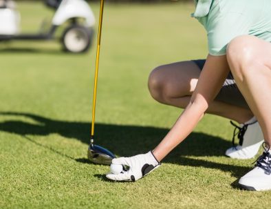 Low section of woman holding golf ball while crouching on field